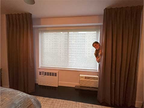 A woman standing behind a set of curtains next to a large window